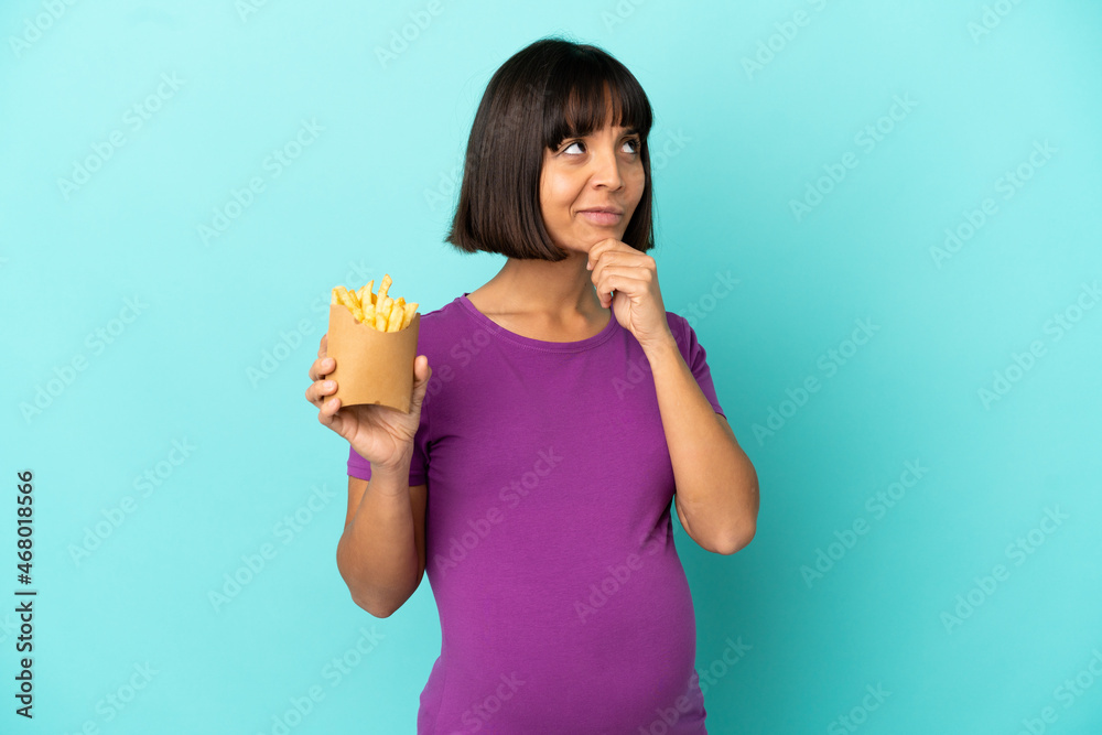 Pregnant woman holding fried chips over isolated background having doubts and thinking Pregnant woman holding fried chips over isolated background having doubts and thinking