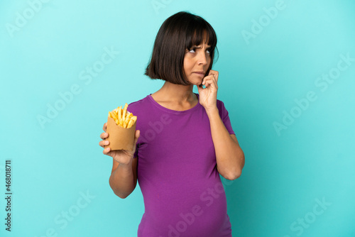 Pregnant woman holding fried chips over isolated background having doubts