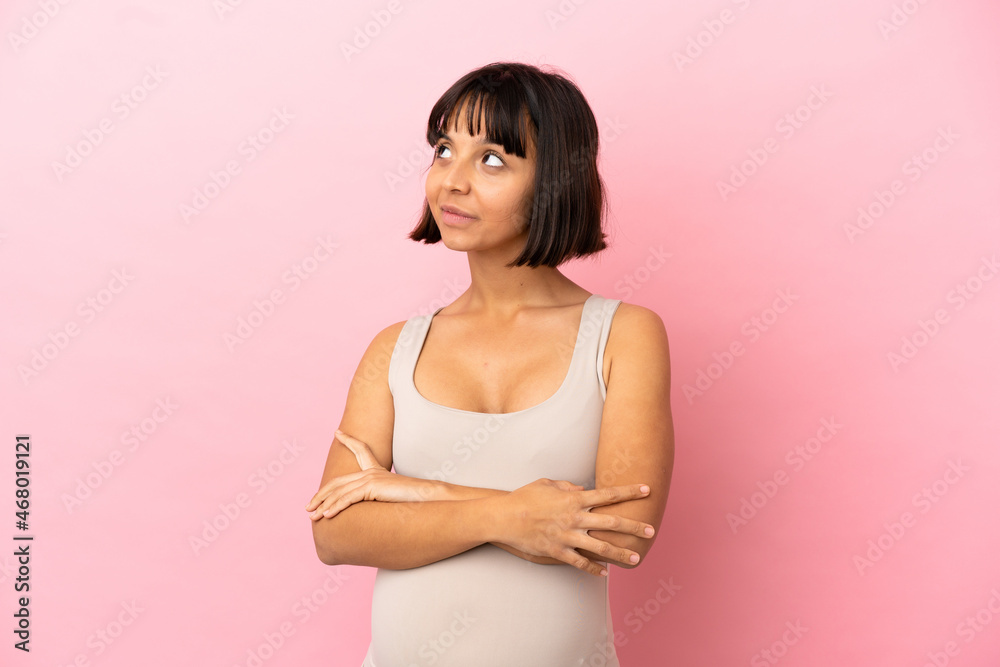 Young pregnant woman over isolated pink background looking up while smiling Young pregnant woman over isolated pink background looking up while smiling