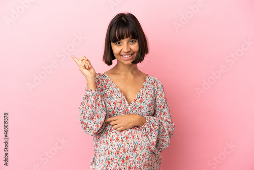 Young pregnant woman over isolated pink background happy and pointing up © luismolinero