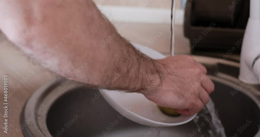 Close up mans hands washing dishes on the modern kitchen sink. Man cleaning plate. Side view Close up mans hands washing dishes on the modern kitchen sink. Man cleaning plate. Side view