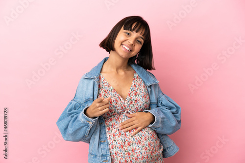 Young pregnant woman over isolated pink background pointing front with happy expression © luismolinero