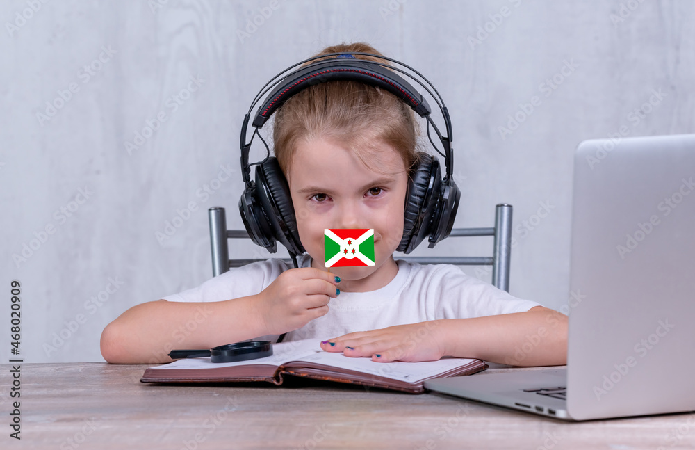 School female child with Burundi flag. Child in headphones, with a book and laptop has lesson online School female child with Burundi flag. Child in headphones, with a book and laptop has lesson online