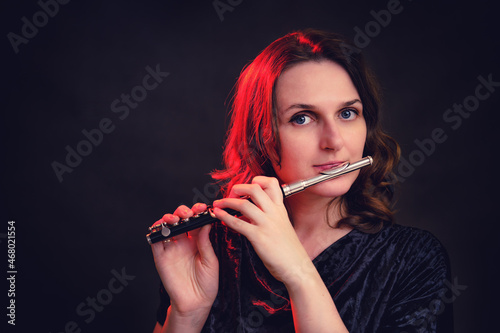 Portrait of a woman musician with a piccolo flute on a studio black background. Flutist with a small flute in her hands photo