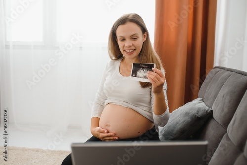 selective focus of cheerful pregnant woman showing ultrasound photos while having video call © Serhii