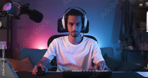 Young Asian man turn chair around, start playing online computer video game, colorful lighting broadcast streaming live at home. Gamer lifestyle, E-Sport online gaming technology concept photo