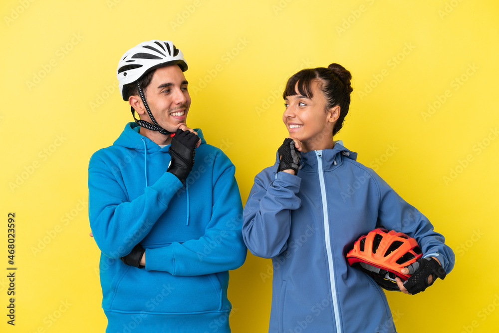 Fototapeta premium Young cyclist couple isolated on yellow background looking looking at each other