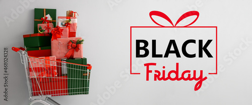 Shopping cart with heap of gifts and text BLACK FRIDAY on light background