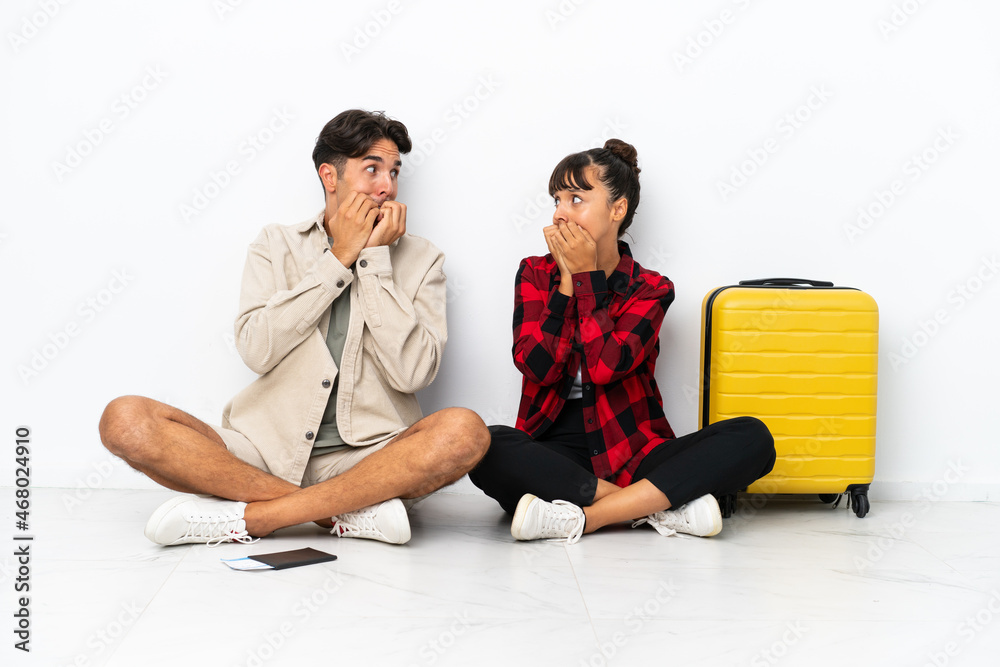 Young mixed race travelers couple sitting on the floor isolated on white background is a little bit nervous and scared putting hands to mouth Young mixed race travelers couple sitting on the floor isolated on white background is a little bit nervous and scared putting hands to mouth