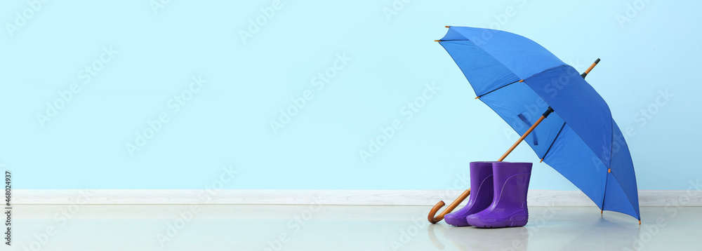 Pair of rubber rain boots and umbrella on color background with space