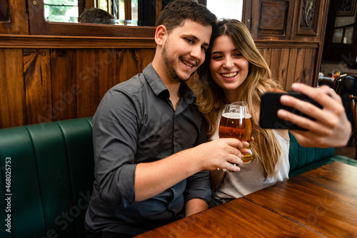 Canvas Print cute and young man and woman couple sitting down at indoor pub having fun, takin