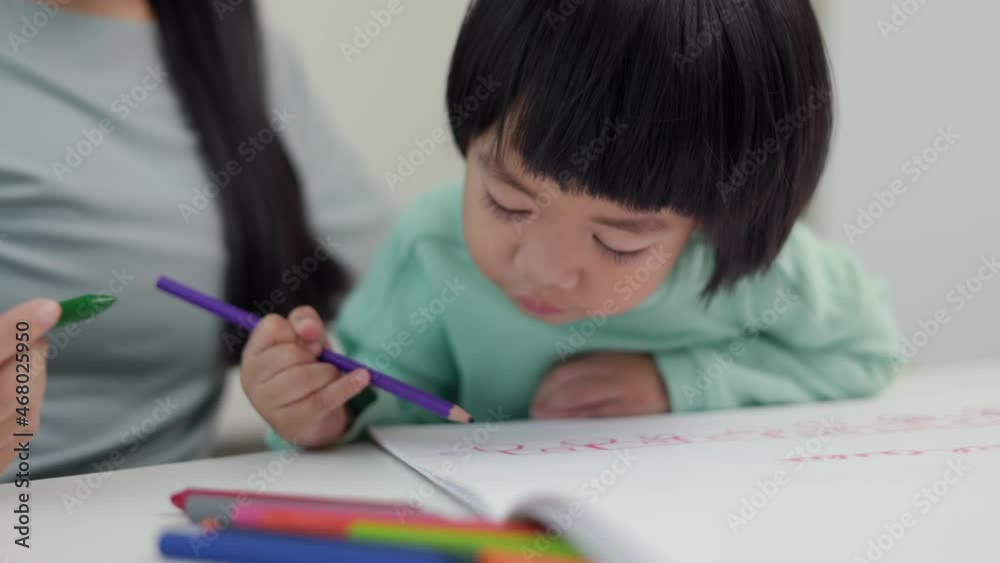 Mom teaching son how to painting with crayon color on book or doing homework. Happy asian boy painting with crayon and colored pencil with his mother in living room at home. family concept. Mom teaching son how to painting with crayon color on book or doing homework. Happy asian boy painting with crayon and colored pencil with his mother in living room at home. family concept.