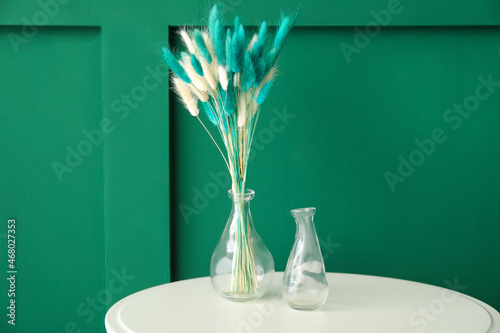 Vase with beautiful dried flowers on white table against color background photo