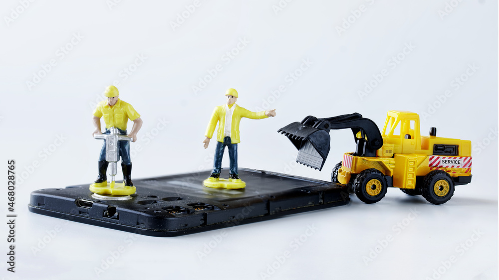 Toy man workers repair or dispose of an old mobile phone or smartphone using a jackhammer and a forklift truck. Smartphone repair or recycling concept. Micro world Toy man workers repair or dispose of an old mobile phone or smartphone using a jackhammer and a forklift truck. Smartphone repair or recycling concept. Micro world