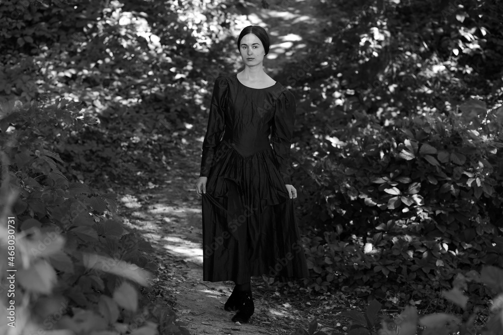 Woman in dress standing on a path in the forest in black and white Woman in dress standing on a path in the forest in black and white