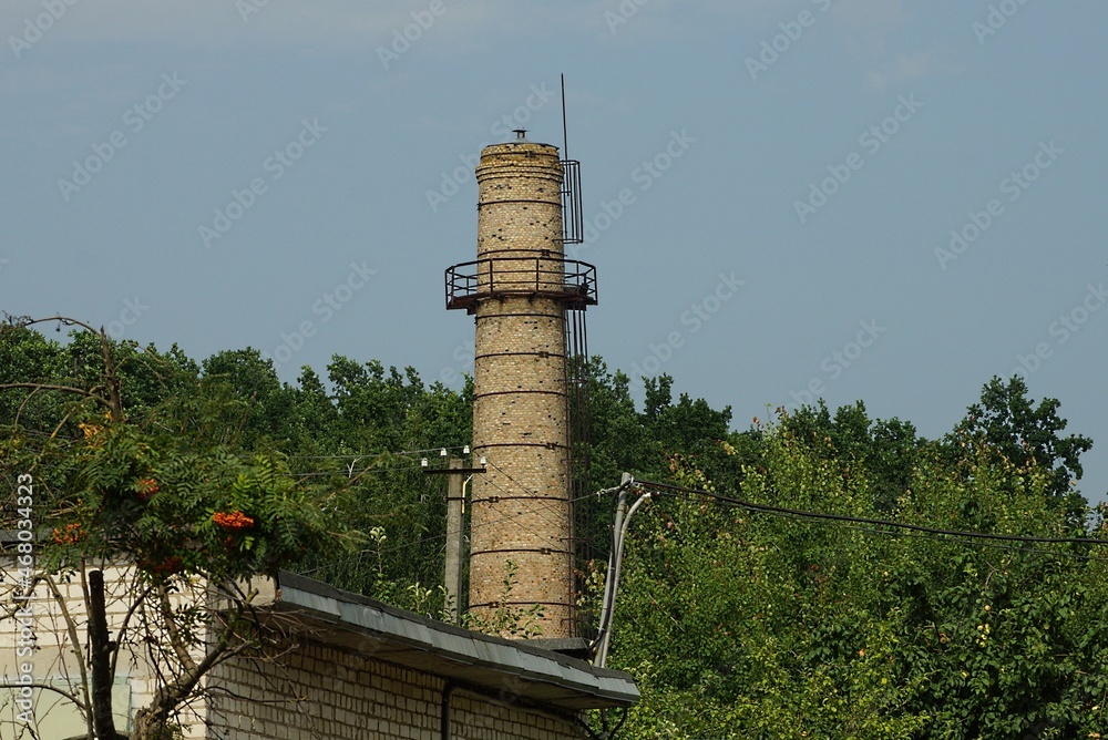 Fototapeta premium one old tall brown brick water tower on the street against a background of sky and green trees