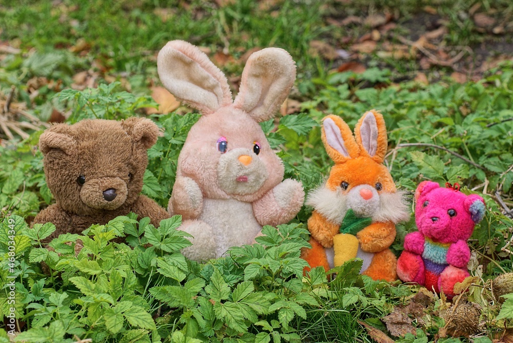 four colored plush toys made of hares and bears stand on the grass and green leaves in the garden four colored plush toys made of hares and bears stand on the grass and green leaves in the garden