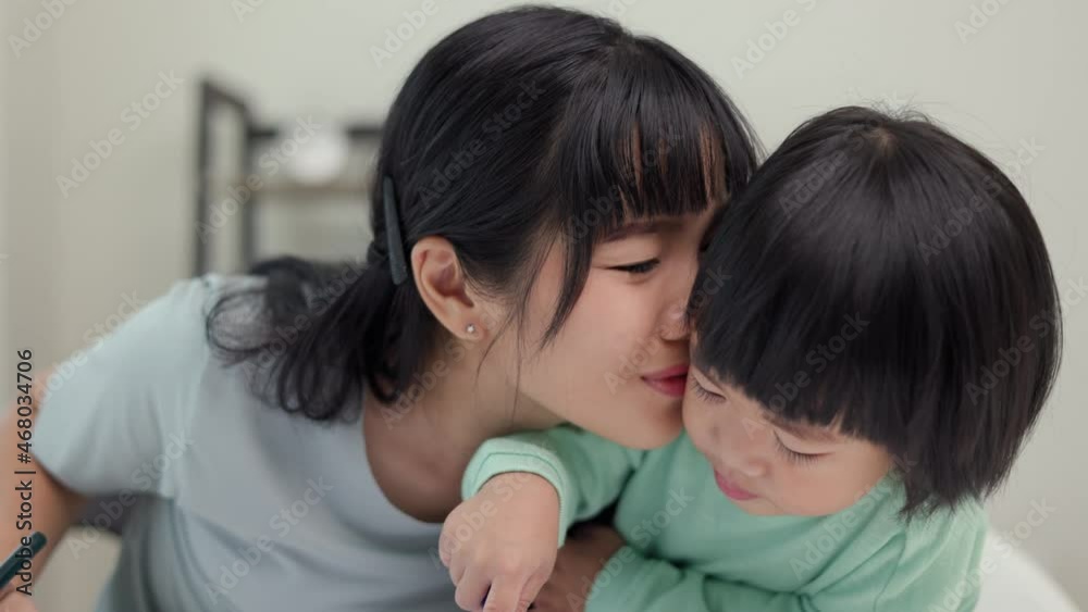 Mom kissing son and teaching how to painting with crayon color on book or doing homework. Happy asian boy painting with crayon with his mother in living room at home. Family having fun concept. Mom kissing son and teaching how to painting with crayon color on book or doing homework. Happy asian boy painting with crayon with his mother in living room at home. Family having fun concept.