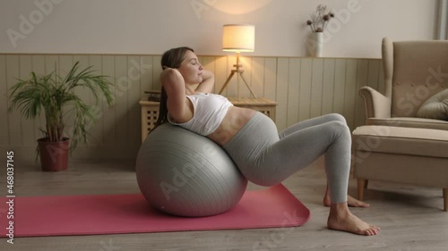 Horizontal shot of attractive pregnant woman with close eyes doing exercises on fitness ball in living room at home. Happy healthy pregnant concept 4k