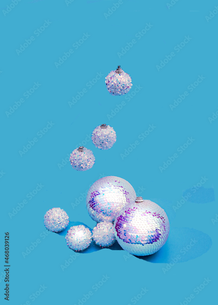 Shiny holographic Christmas balls on pastel blue background, others are falling from above. Festive trendy flashy New Year celebration creative concept. Design for fashion advertisement or banner.