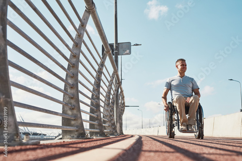 Full length portrait of adult man in wheelchair in accessible city environment outdoors in sunlight, copy space photo