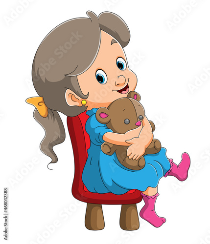 The little girl is holding a doll and sitting on the chair