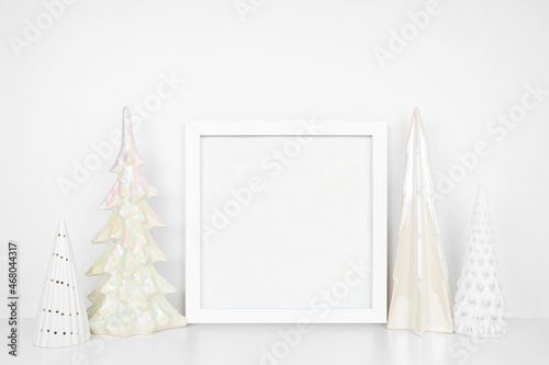 Christmas mock up with white frame and shiny glass tree decor. Square frame on a white shelf against a white wall. Copy space. © Jenifoto