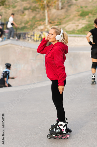 Fit blonde woman with inline skates and headphones standing in a skate park