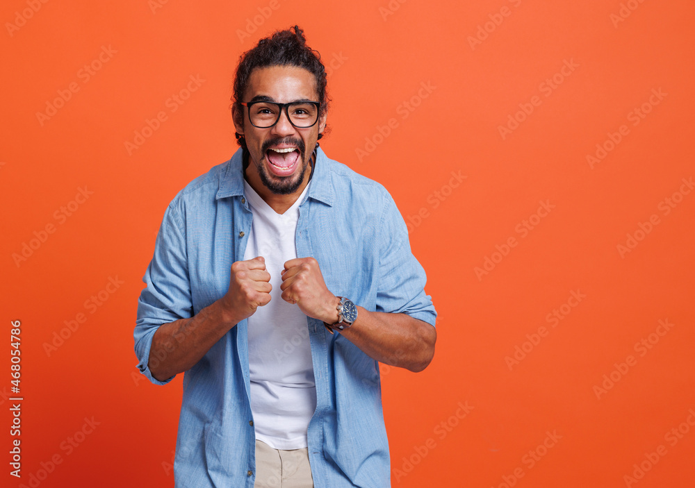 Excited young african american man winner raising arms with clenched fists and celebrating success