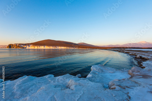 Colorful sunset on the snowy coast of the Sea of Japan. The Sonce goes over the snowy hills against the backdrop of the calm sea. Sikhote-Alin Biosphere Reserve in the Primorsky Territory. photo