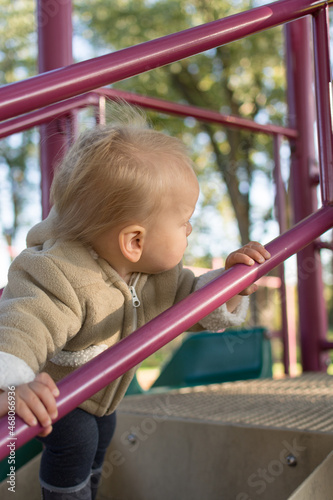 16 month old climbing stairs at a playground in the fall; purple railing being grasped for support