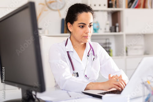 Portrait of therapist woman who is sitting behind laptop in clinic