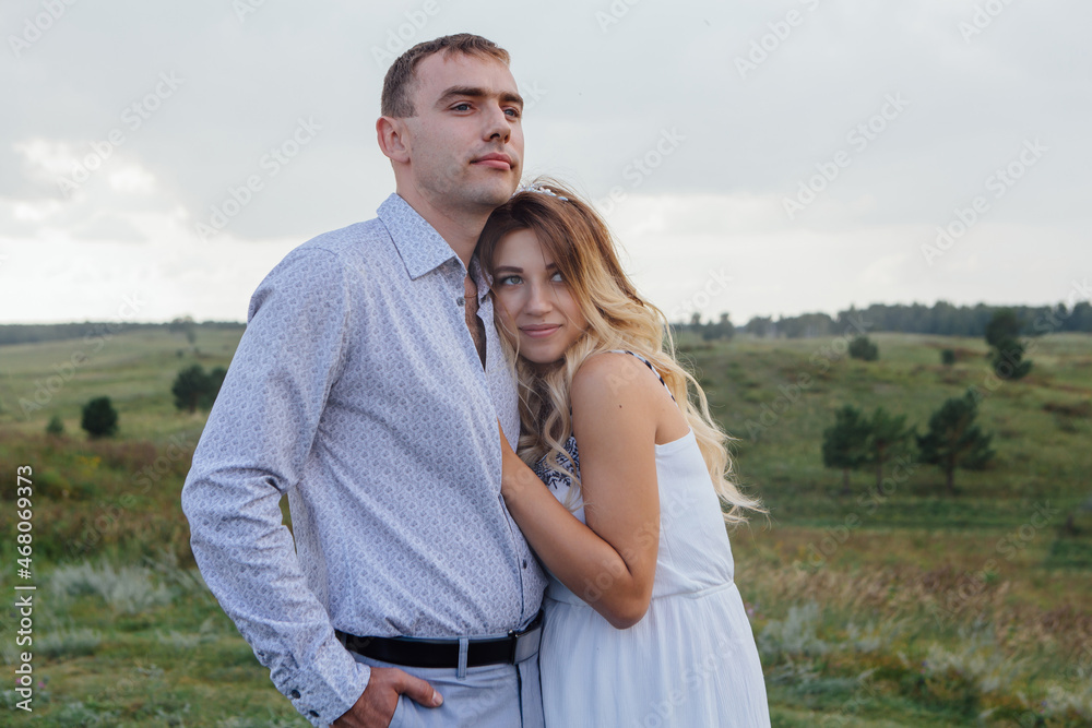 Happy young couple, expecting a baby. Pretty pregnant woman in a white dress hugs her man outdoors. Happy young couple, expecting a baby. Pretty pregnant woman in a white dress hugs her man outdoors.