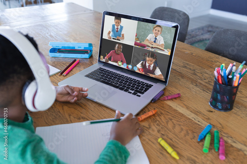 African american boy using laptop for video call, with diverse elementary school pupils on screen photo