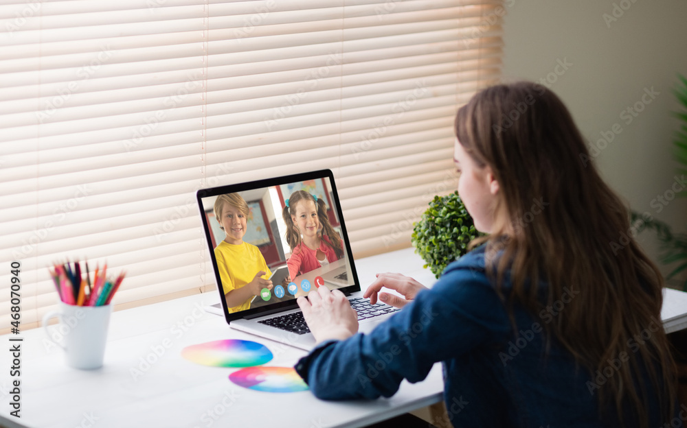 Caucasian girl using laptop for video call, with smiling elementary school pupils on screen Caucasian girl using laptop for video call, with smiling elementary school pupils on screen