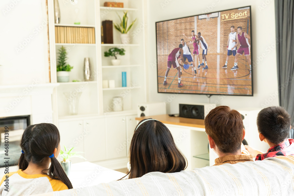 Rear view of family sitting at home together watching basketball match on tv Rear view of family sitting at home together watching basketball match on tv