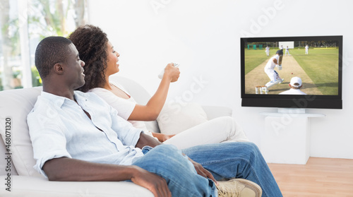 Rear view of african american couple sitting at home together watching cricket match on tv