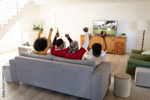 Rear view of family sitting at home together watching football match on tv