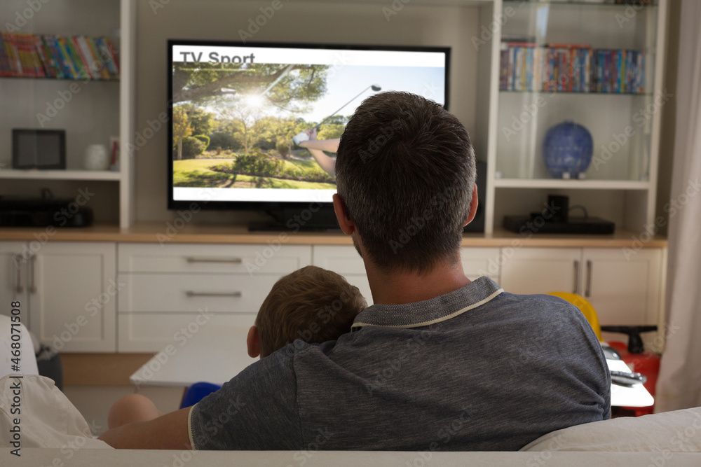 Rear view of father and son sitting at home together watching sport event on tv Rear view of father and son sitting at home together watching sport event on tv