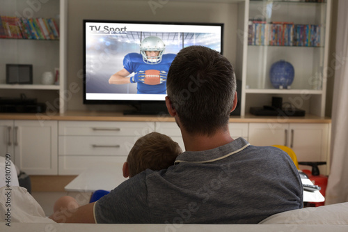 Rear view of father and son sitting at home together watching sport event on tv © vectorfusionart