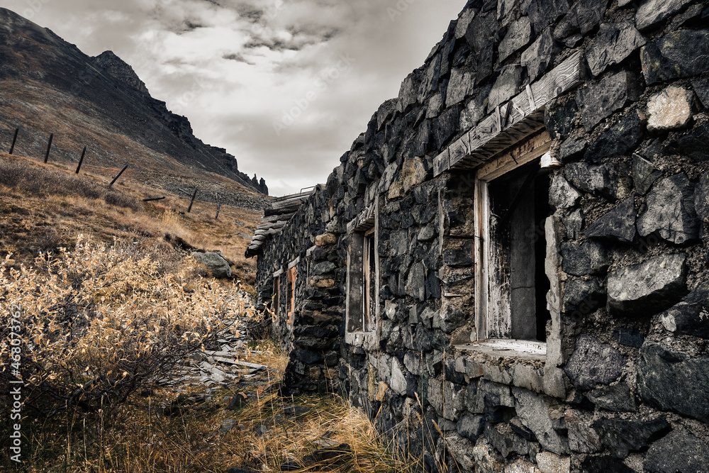 An old abandoned stone building at the foot of the mountain. Harsh arctic landscape. Soviet warehouse building. Barbed wire fence and rocks in the distance. Environs of Egvekinot, Chukotka, Russia.