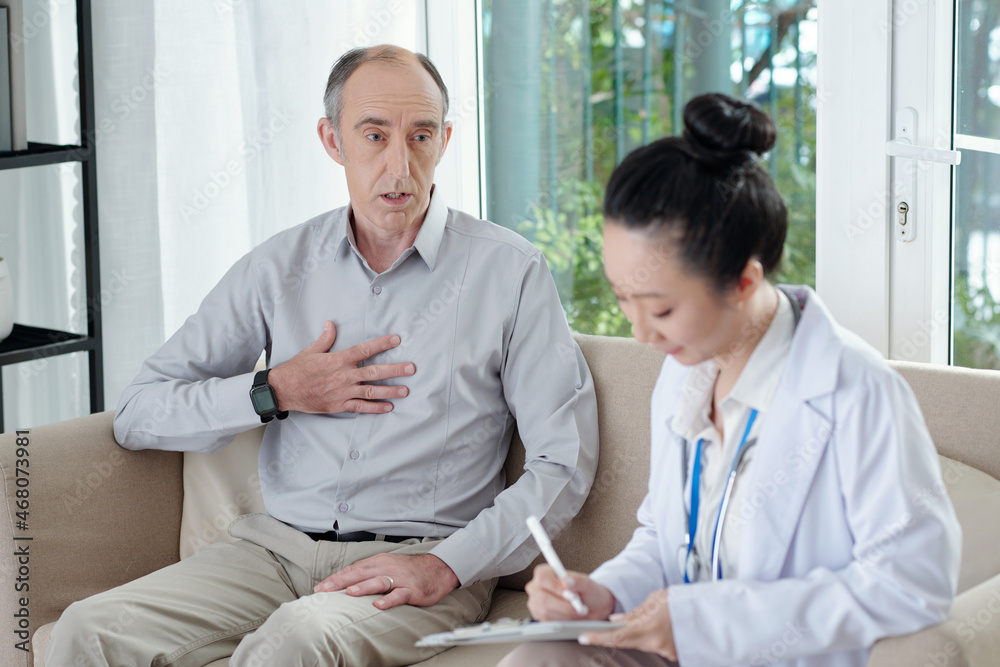 Senior man complaining about tachycardia when talking to doctor visiting him at home