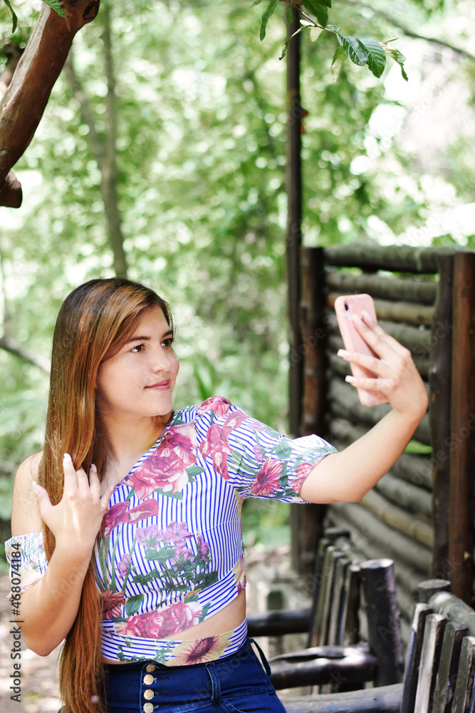 Fototapeta premium Mujer joven tomándose una fotografía con el teléfono o haciendo una videollamada. Mujer Guatemalteca en un ambiente natural.