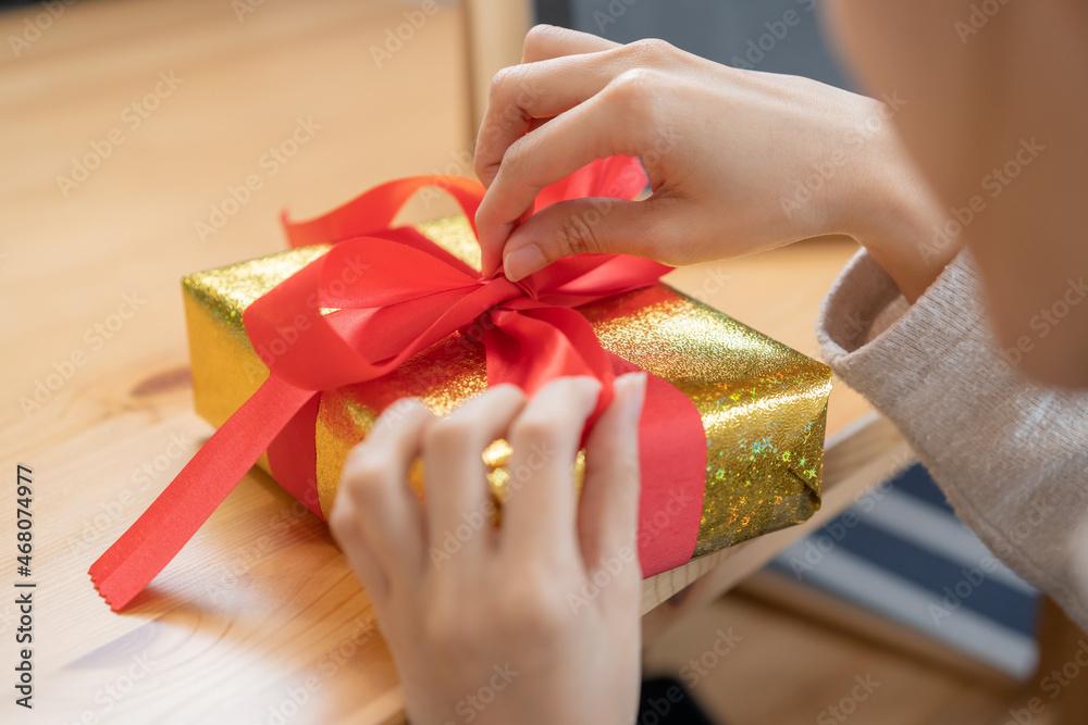 Christmas eve festival season, hand of asian young woman, girl wrapping gold gift box with red ribbon or bow on table at home, happy to get present on merry xmas day. Celebration on New Year festival. Christmas eve festival season, hand of asian young woman, girl wrapping gold gift box with red ribbon or bow on table at home, happy to get present on merry xmas day. Celebration on New Year festival.