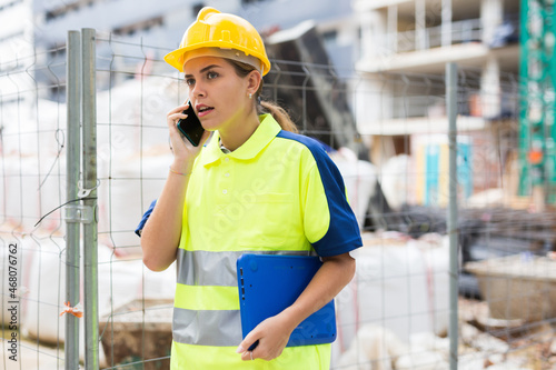 Young confident woman working as a process engineer on a construction site discusses important issues on a mobile phone