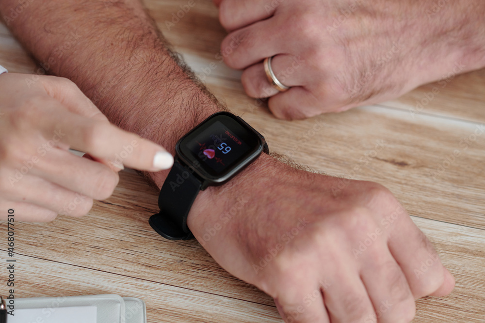 Obraz premium Close-up image of caregiver showing senior man how to check his heart rate via app on smartwatch