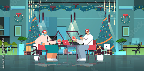 podcasters in santa hats talking to microphones recording podcast in decorated studio new year christmas holidays celebration