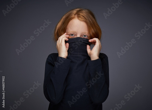 red-haired girl with freckles on her face in a black sweater posing