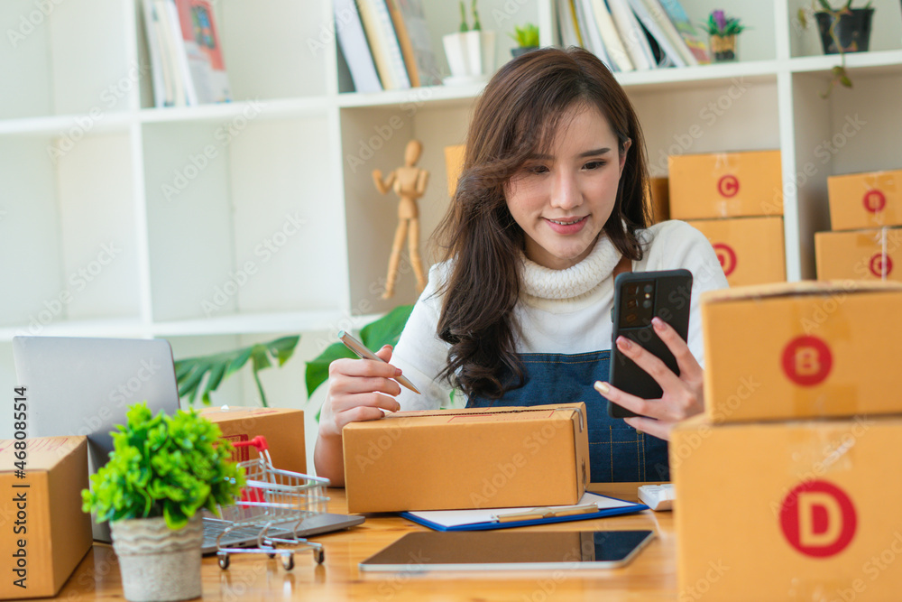 Young Asian woman entrepreneur working at home office, BOX,smartphone,laptop, online, marketing, packaging, delivery, SME, e-commerce concept. Young Asian woman entrepreneur working at home office, BOX,smartphone,laptop, online, marketing, packaging, delivery, SME, e-commerce concept.