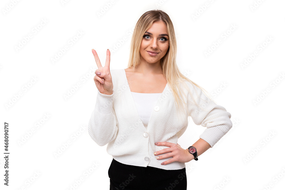 Photo of a beautiful attractive pretty amazing charming young blonde woman with makeup in a stylish white knitted sweater and black pants shows two fingers isolated on a white background with empty Photo of a beautiful attractive pretty amazing charming young blonde woman with makeup in a stylish white knitted sweater and black pants shows two fingers isolated on a white background with empty